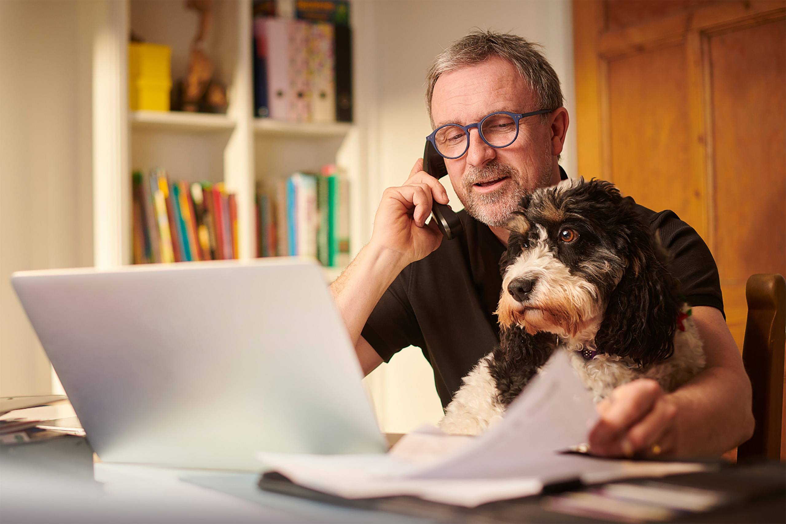 Man talking on the phone beside his dog at a computer deesk
