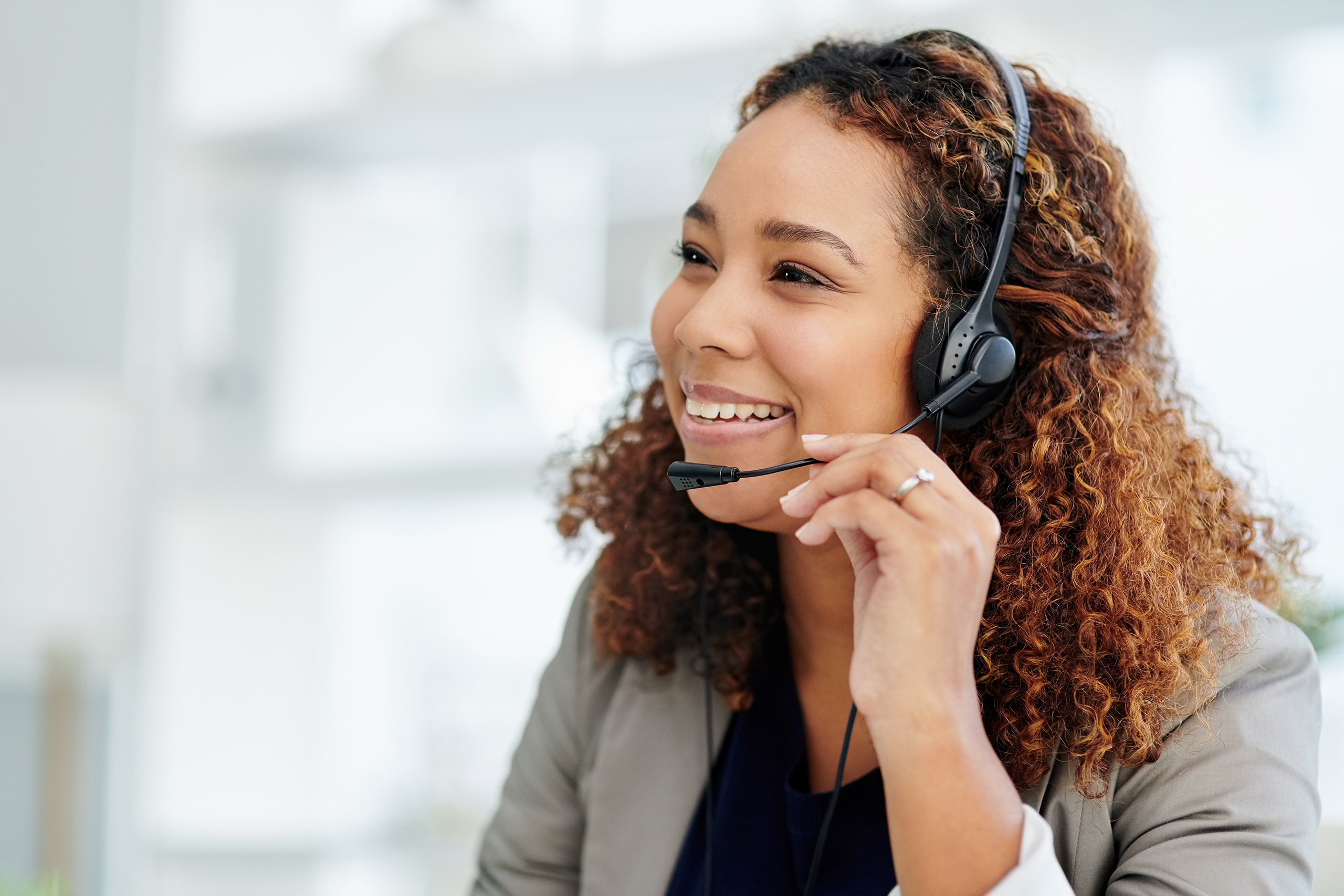 Woman. with brown curly hair talking on a black headset in a bright room