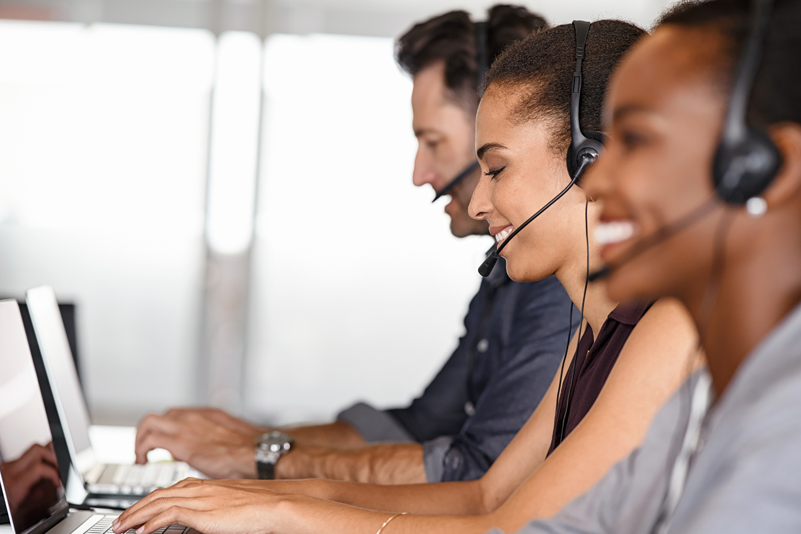 Three people wearing headsets, answering calls and using their computers