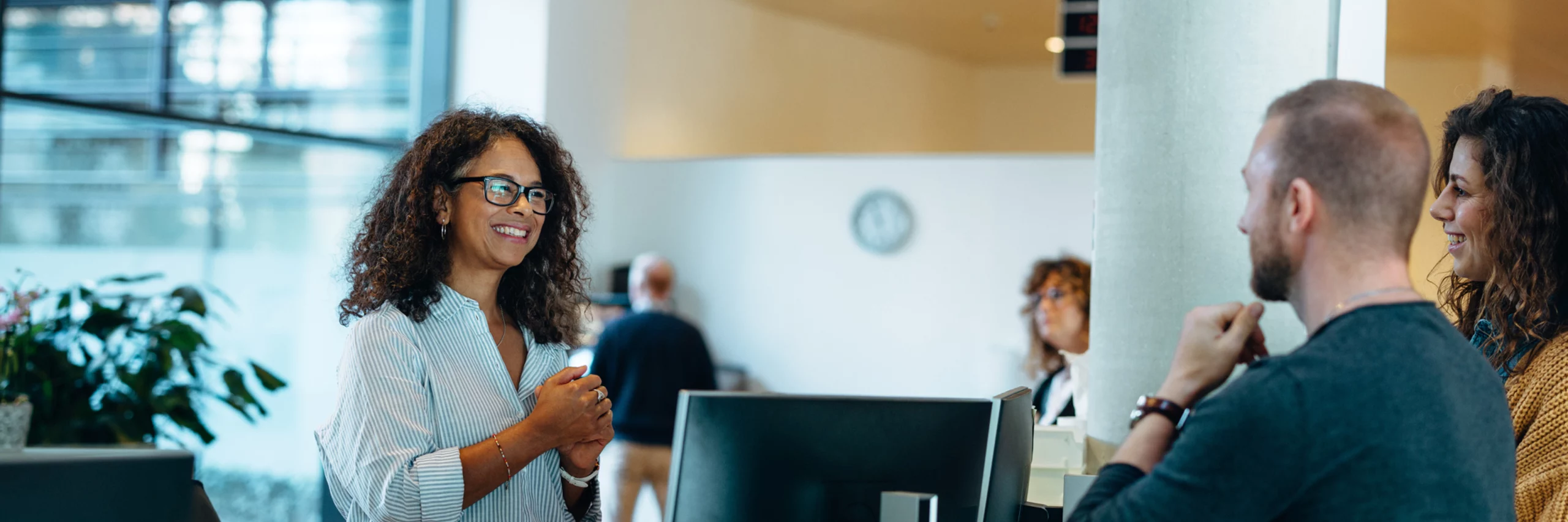 BIPOC woman with glasses and curly hair talking to a couple