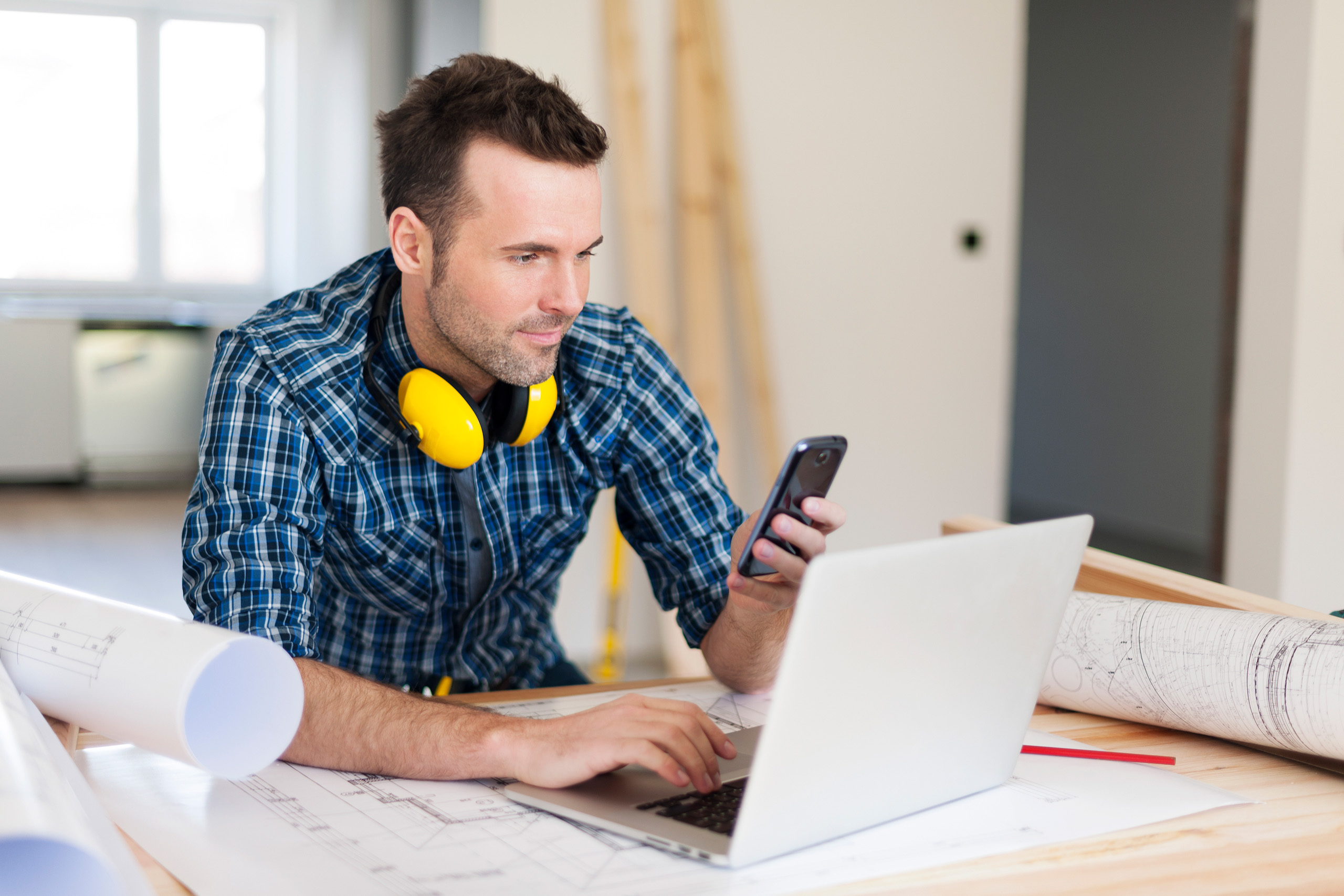 Young caucasian man in blue plaid shirt, working on his laptop an cell phone